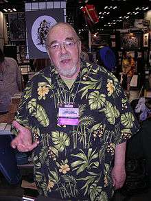 A man in his late sixties. He has a beard, glasses, and is wearing a Hawaiian shirt.