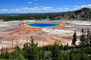 Pool of blue water surrounded by orange and yellow residue, in ashen rock basin.