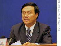 a serious looking man with a long haircut, wearing a white shirt, a suit and a blue tie with white stripes