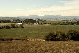 Farm fields spread into the distance, where a barn and far-off mountains can be seen